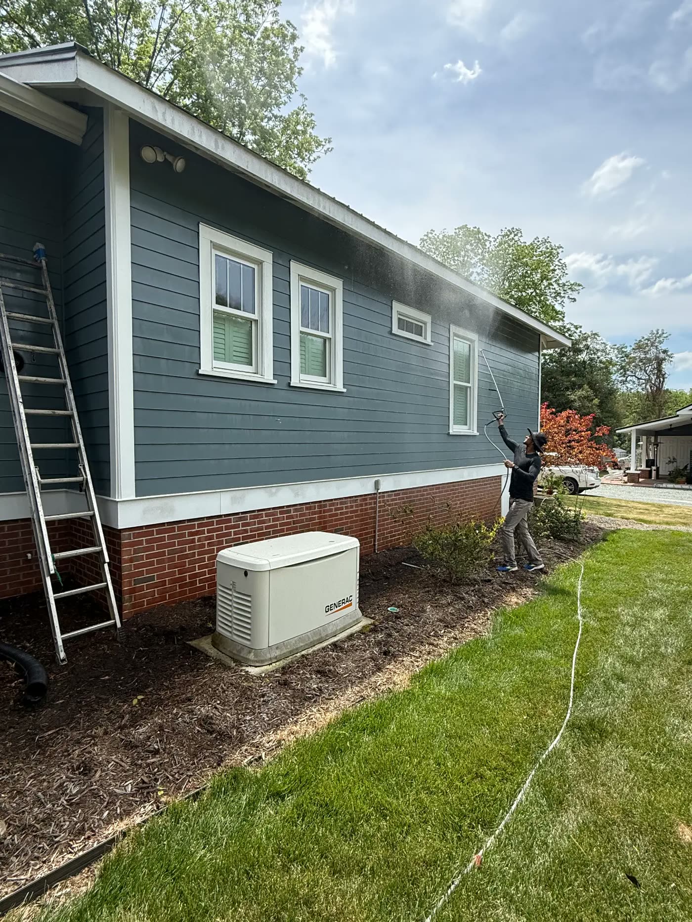 Technician pressure washing the siding of a blue-gray home