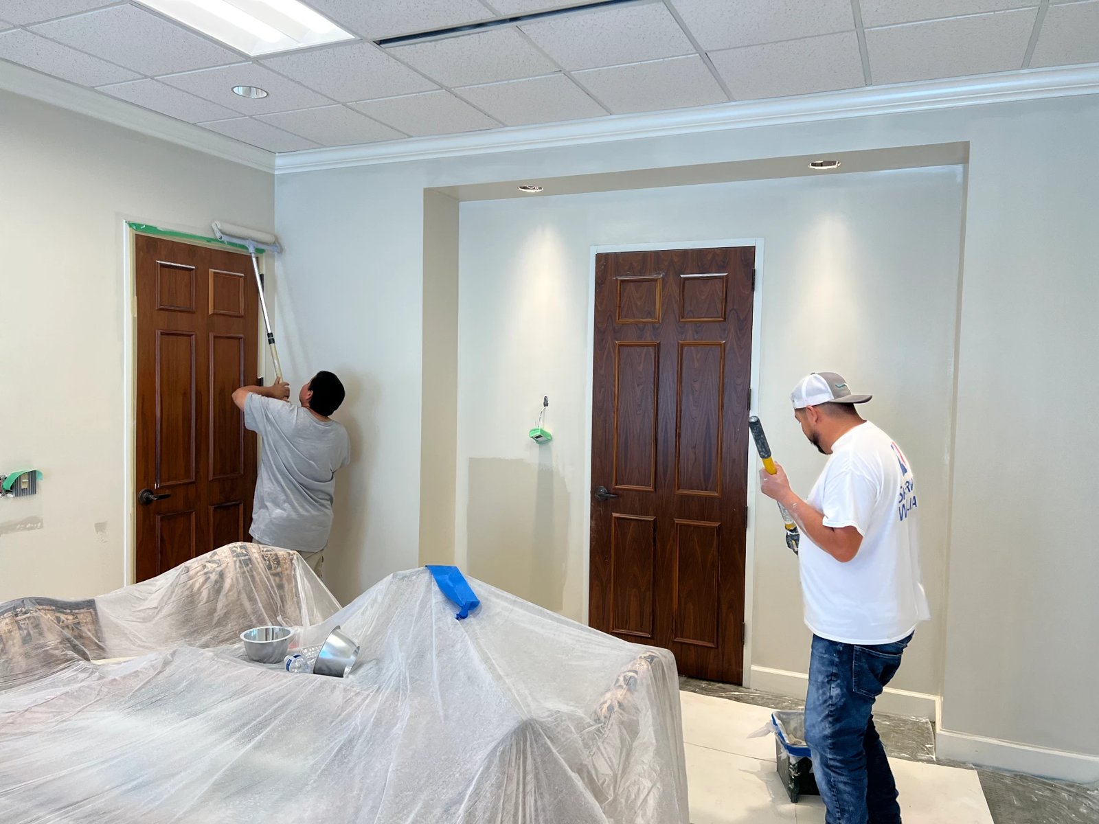 Painters cutting in walls and trim around wood doors in an office