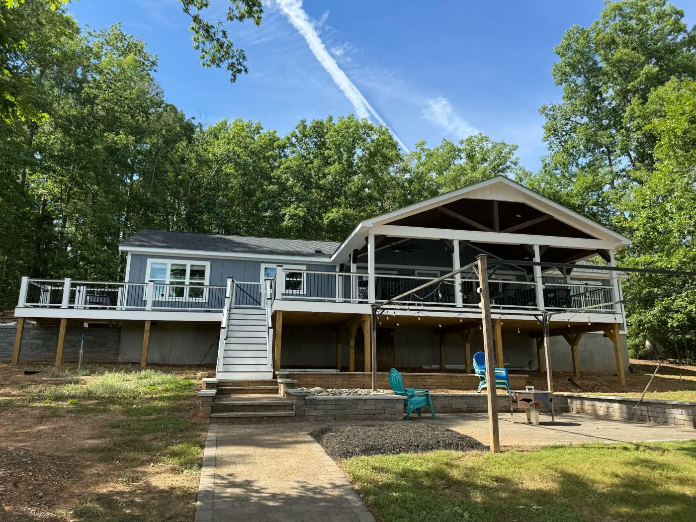 Gray lake house with white trim, covered porch and freshly finished wraparound deck
