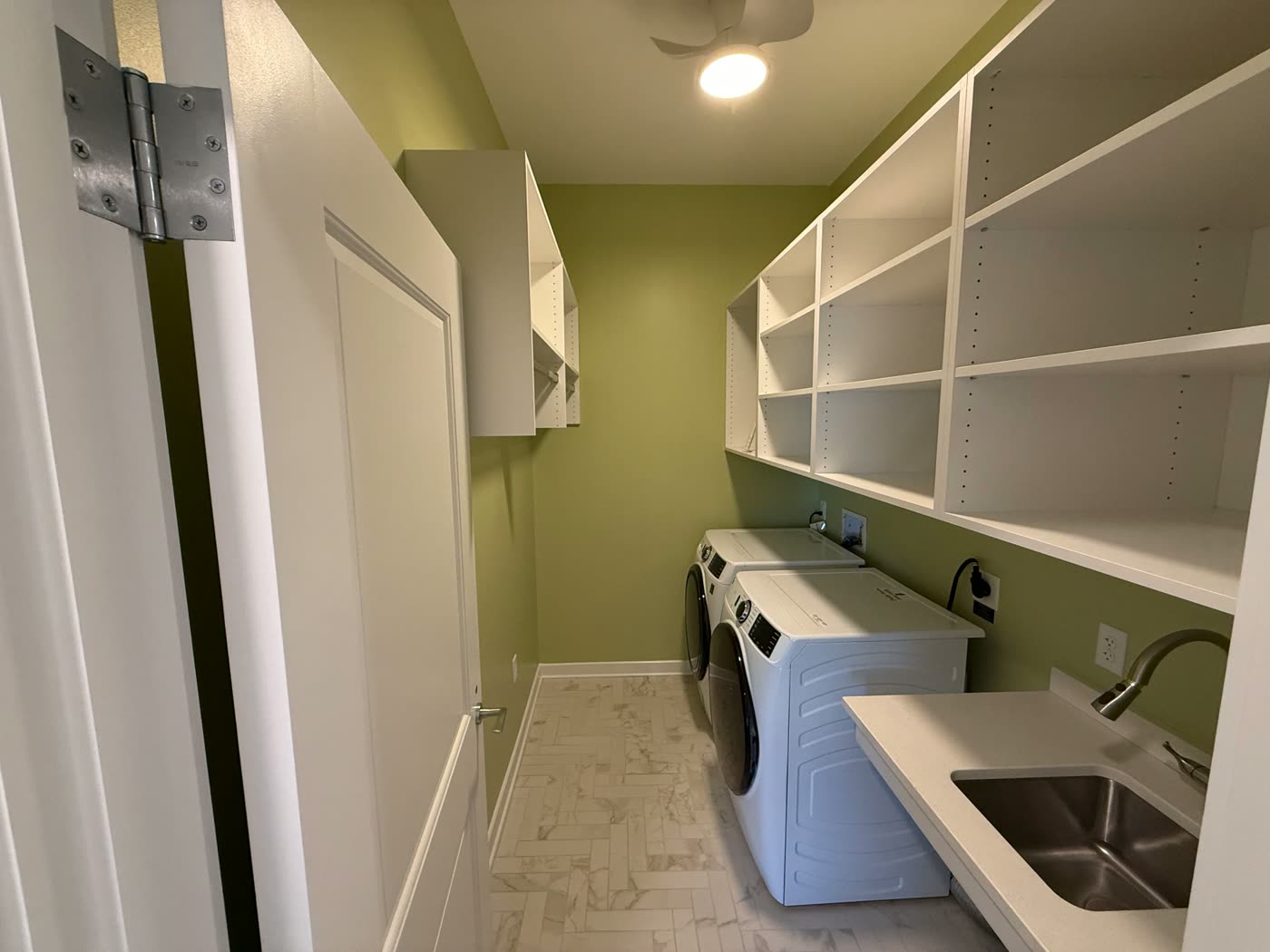 Laundry room painted in a soft green with white cabinetry and trim